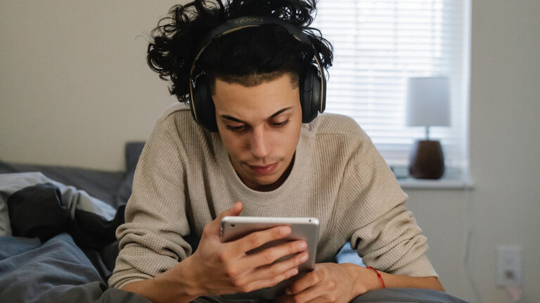 Young Latinx man wearing headphones and looking at a tablet with concentration.