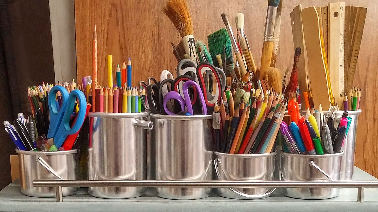A variety of art supplies in bucket, such as colored pencils, scissors, brushes, rulers, and markers.
