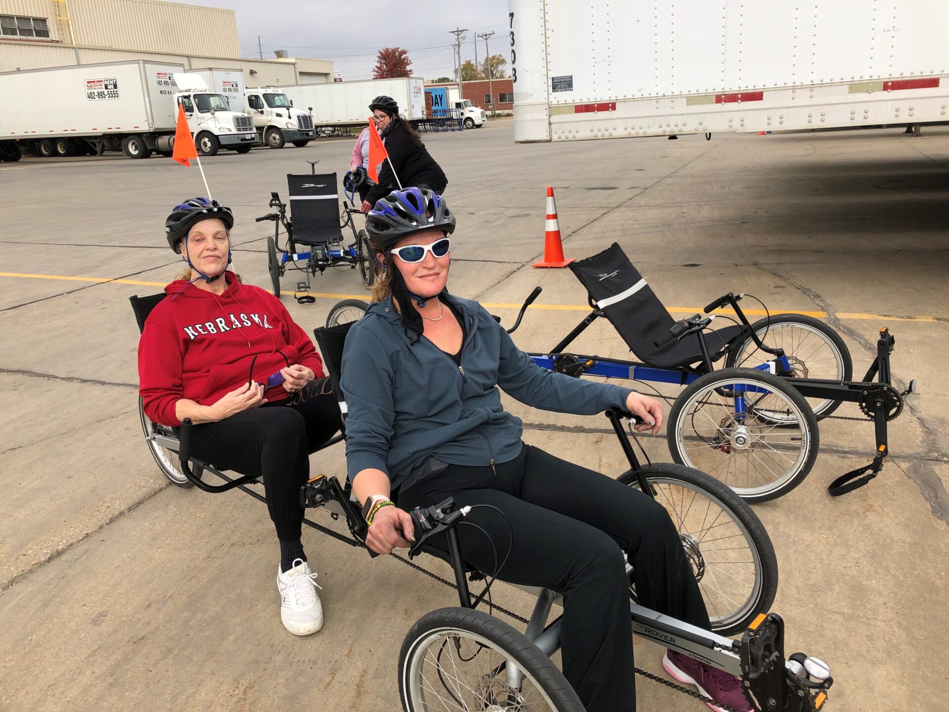 Two women with bike helmets on smiling and sitting on a tandem recumbent bike.