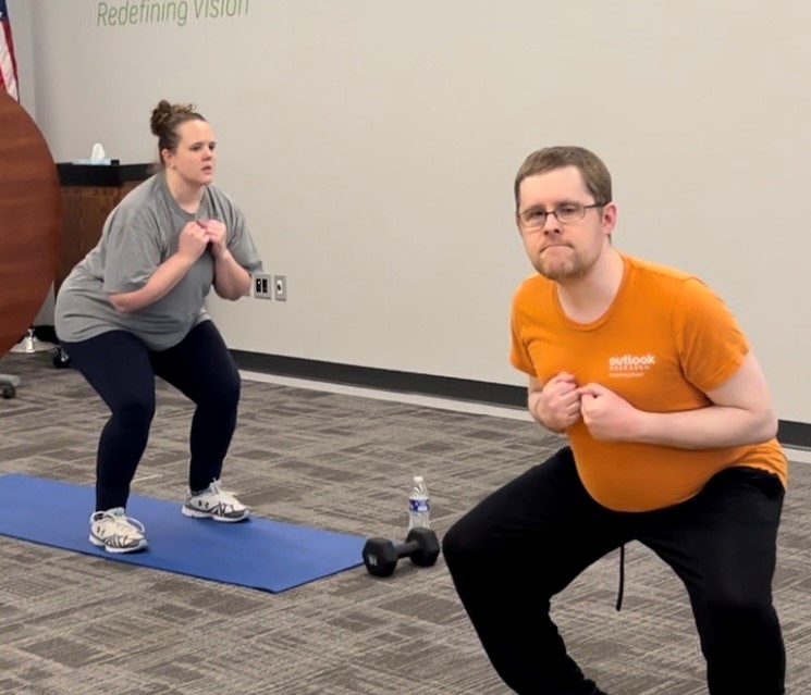 a woman and a man in a workout class, They are both in a squatting position