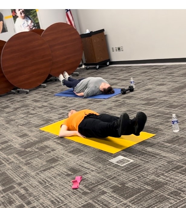 A man and a woman laying on their backs on yoga mats. Their legs are raised off the ground about 5 inches.