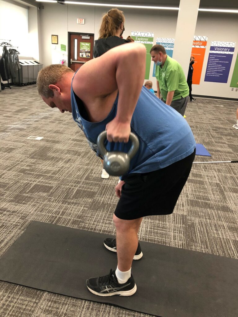 A man is bent at the waist doing a rowing motion with a kettle bell in one hand.