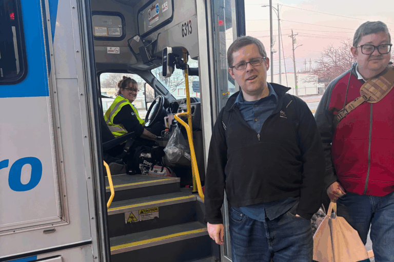 Aaron and Ben are standing in front of the MOBY bus, smiling. The female bus driver is smiling too.